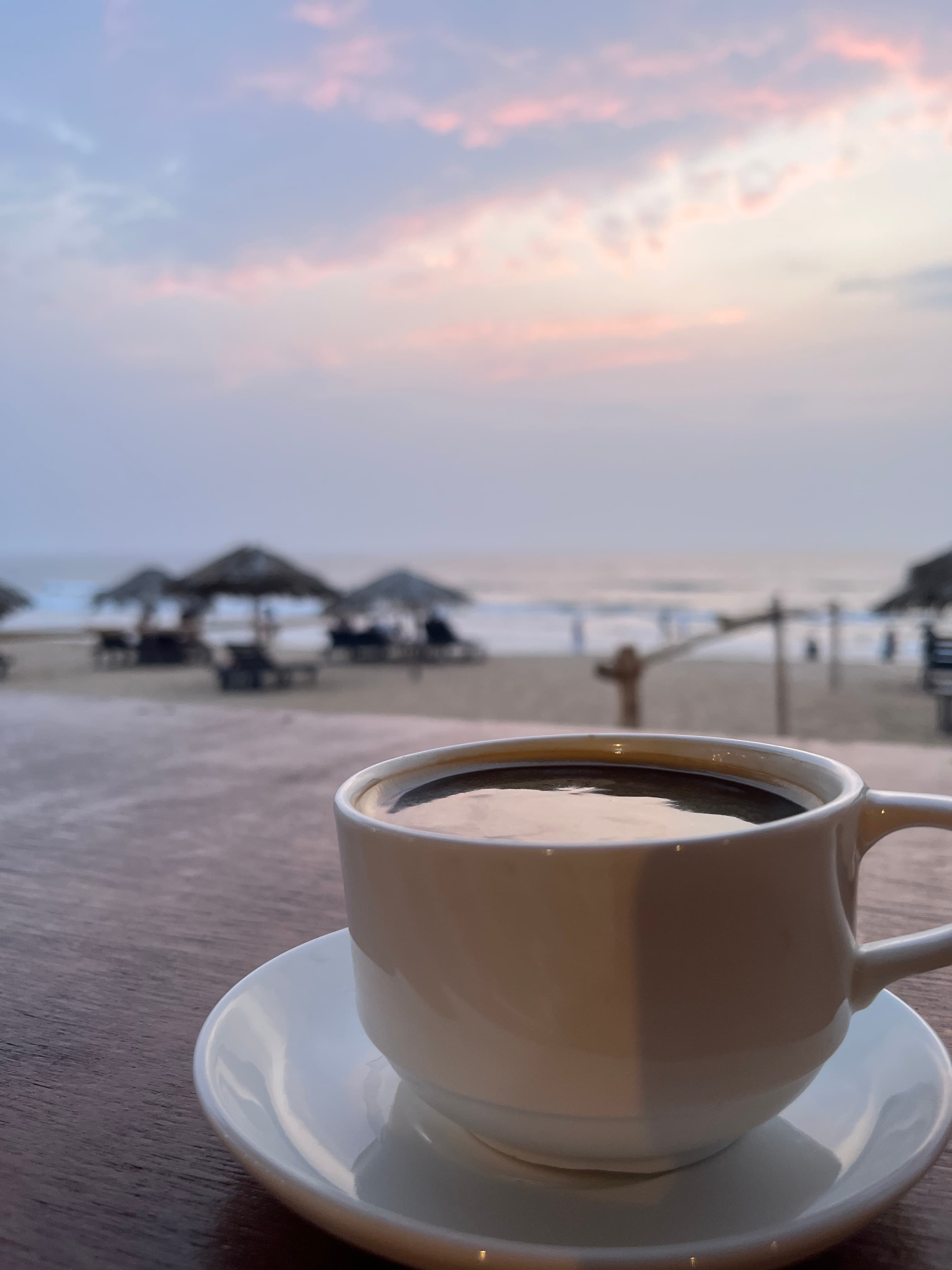 Cup of coffee on a table with the beach and palapas in soft focus behind